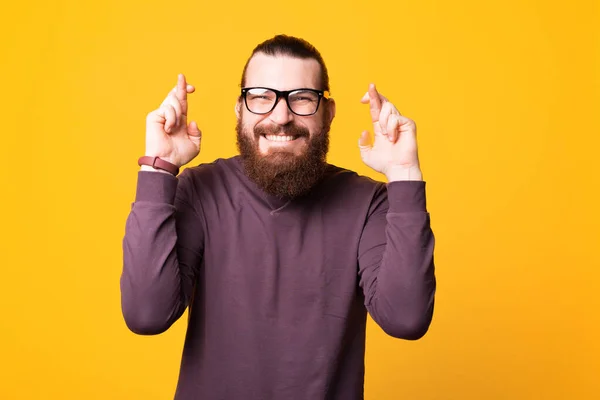 Un joven barbudo excitado con gafas espera que sus sueños se hagan realidad cerca de una pared blanca — Foto de Stock