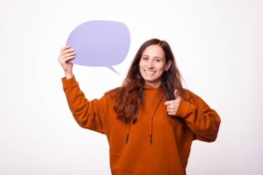 Genç bir kadın kameraya gülümsüyor ve elinde bir konuşma balonu tutuyor.