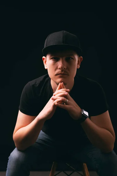 A serious young hipster is sitting on a chair looking at the camera — Stock Photo, Image