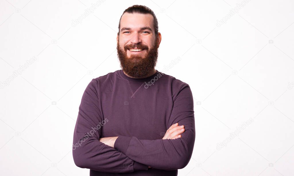 Bearded man is smiling at the camera and sitting with his arms crossed