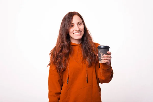Fröhliche junge Frau hält eine Tasse mit Heißgetränk in der Hand und lächelt in die Kamera — Stockfoto