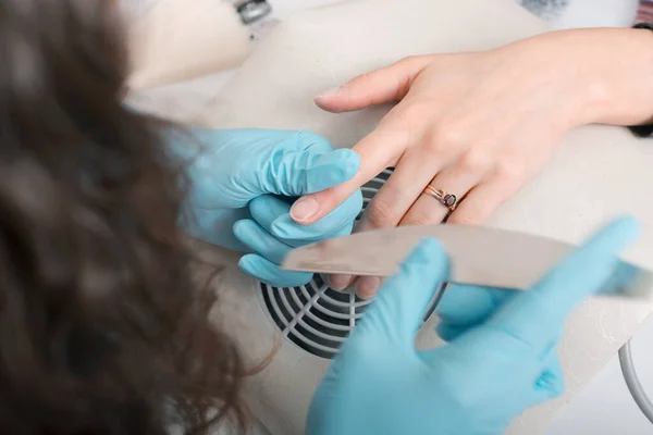 Um mestre de unhas no salão está lustre clientes unha com um arquivo de unhas — Fotografia de Stock