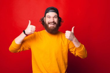 Heyecanlı genç bir adam iki parmağını da kaldırıyor ve kameraya gülümsüyor.