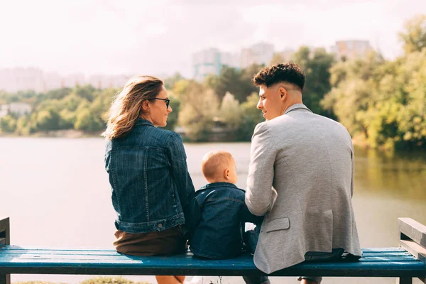 Picture of a young family in park looking at each other near a lake on a bench — Stock Photo, Image