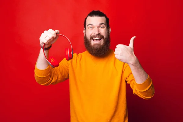 Foto eines bärtigen jungen Mannes mit Kopfhörern und Daumen hoch lächelt in die Kamera — Stockfoto