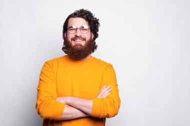 Gözlüklü genç sakallı bir adamın portresi kollarını kavuşturarak kameraya bakıyor.