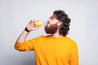 Beyaz duvardan su içen sakallı genç adamın fotoğrafı.