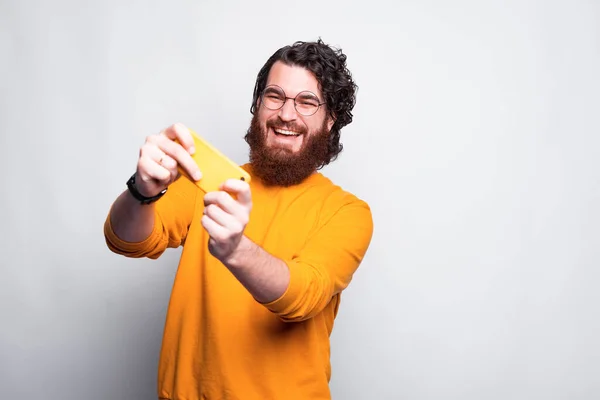 Fotografie veselý mladý vousatý hipster muž hrát hry na smartphone — Stock fotografie