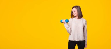 Mutlu genç bir kadın, sarı bir vajinanın yanında bir dambılı kaldırıyor.