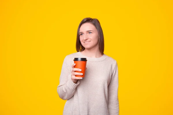Retrato de la mujer joven de pie sobre el fondo amarillo y beber taza de café para ir — Foto de Stock