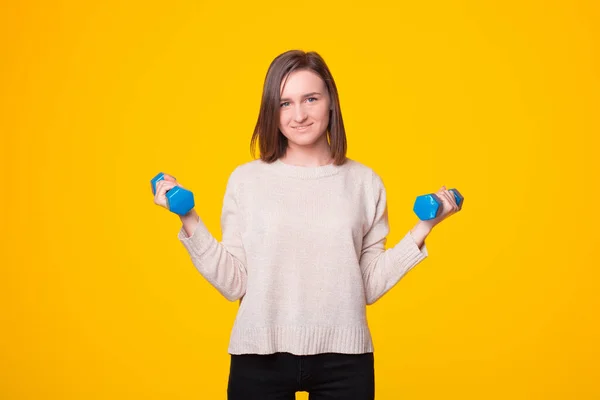 Una joven alegre está mirando a la cámara sonriendo y está haciendo ejercicio con dos pesas — Foto de Stock