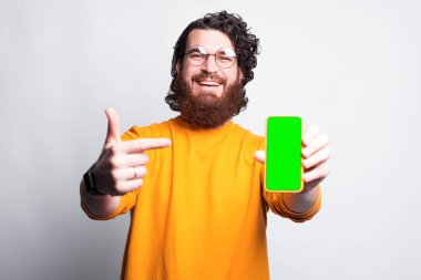 Mutlu genç bir adam kameraya gülümsüyor ve elinde bir telefon var.