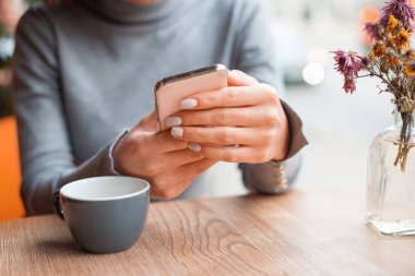 Bir kafede elinde bir fincan kahveyle oturan bir kadının fotoğrafı.