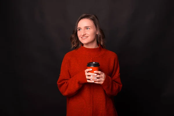 Feliz joven mujer está mirando hacia otro lado y sonriendo está sosteniendo una taza de bebida caliente — Foto de Stock