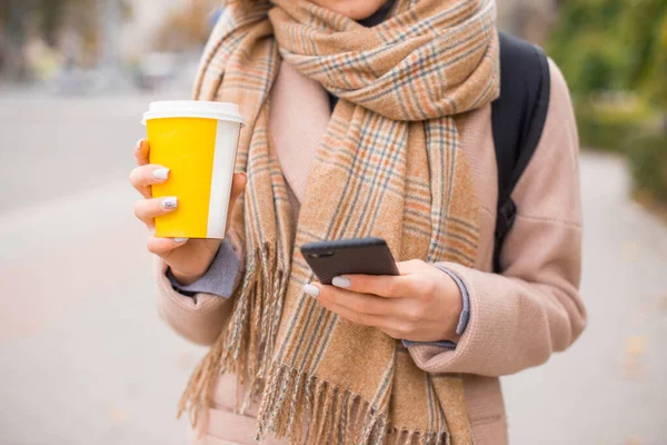 Uma foto de uma mulher segurando uma xícara de bebida quente e seu telefone mensagens — Fotografia de Stock