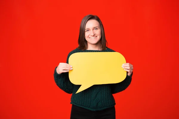 Retrato de mujer alegre sobre fondo rojo sosteniendo burbuja de habla amarilla vacía — Foto de Stock