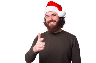 Pozitif sakallı hippi Noel Baba şapkası takıyor ve kamerayı işaret ediyor.