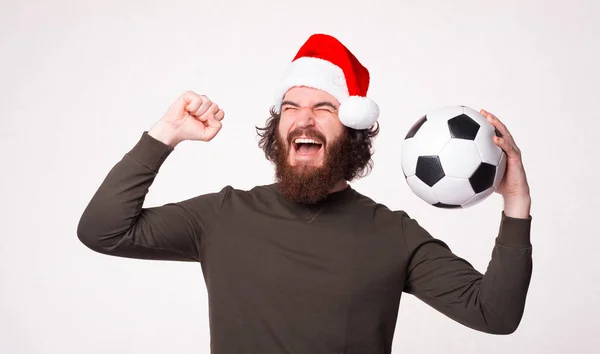 Cheerful bearded hipster man screaming and celebrating victory and holding soccer ball, santa claus — Stock Photo, Image