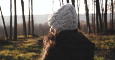 Sonbahar günbatımında ormanda yürüyen beyaz şapkalı genç bir kadın.