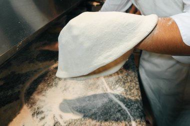 Becerikli şef pizzanın hamurunu elleriyle yuvarlıyor.