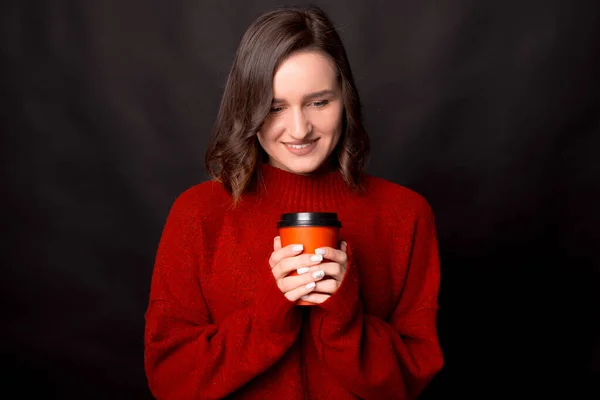 Porträtt av attraktiv brunett kvinna i röd tröja med en kopp varm dryck på mörk bakgrund — Stockfoto