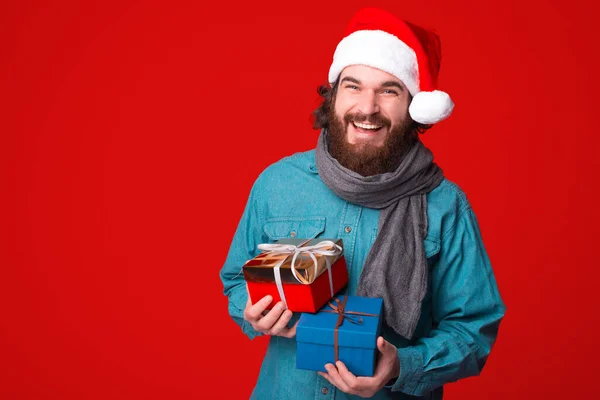 Przystojny brodaty mężczyzna trzyma pudełka na czerwonym tle i wygląda szczęśliwy przed kamerą — Zdjęcie stockowe