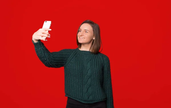 Фото улыбающейся девушки, делающей селфи на смартфоне на красном изолированном фоне — стоковое фото