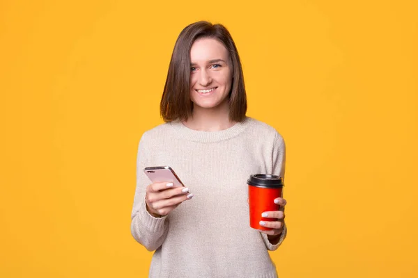 Retrato bela jovem feliz de pé sorriso, segurando telefone celular e xícara de papel de café — Fotografia de Stock