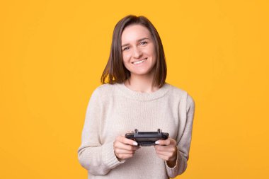 Eğlence zamanı. Sarı arka planda duran kontrol aletini kullanan gülümseyen genç kadının portresi