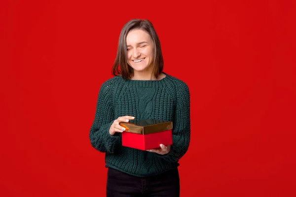 Fröhlich niedliche junge Frau hält eine Geschenkbox, die über rotem isoliertem Hintergrund steht — Stockfoto