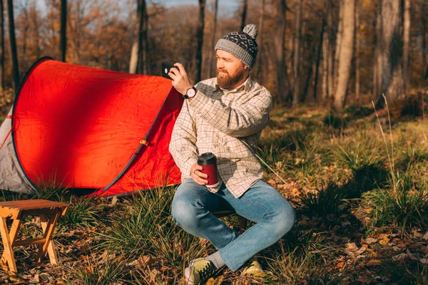 Utomhus fotograferas skäggiga mannen gör foto i skogen med sin smarta telefon. Resenär man vilar efter vandring — Stockfoto