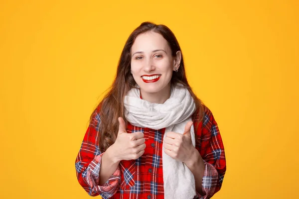 Portret pozytywnej młodej kobiety noszącej szalik i pokazującej kciuki w górę gestu na żółtym tle — Zdjęcie stockowe