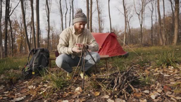 Filmato di barbuto hipster viaggiatore uomo che si prepara per il fuoco nel campo sulla vista tenda — Video Stock