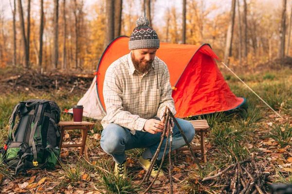 Young man is making a campfire, outdoor in woods in autumn, day time. — Stock Photo, Image