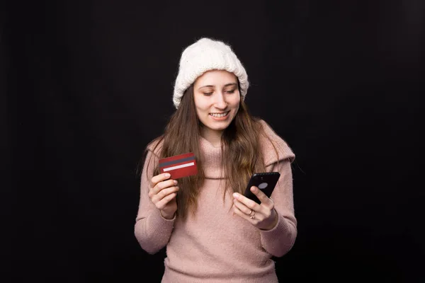 Güzel genç bayan cep telefonu ve kartını siyah arka planda tutarken cep telefonu kullanıyor.. — Stok fotoğraf