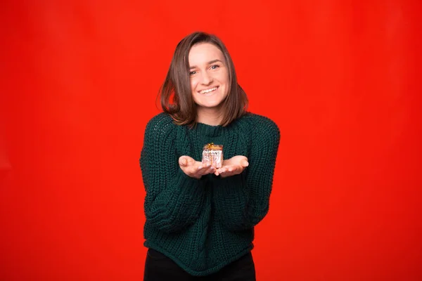 Joven chica bonita está sosteniendo una pequeña caja de regalo sobre fondo rojo. — Foto de Stock