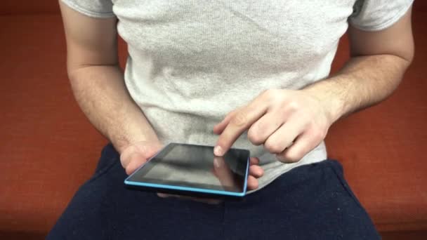 Κλείστε πλάνα του ανθρώπου χρησιμοποιώντας tablet και κάθεται σε πορτοκαλί καναπέ — Αρχείο Βίντεο