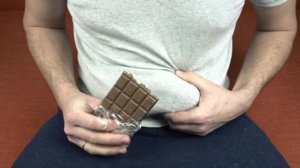 Beelden van een dikke man die chocolade eet met noten en zijn dikke buik aanraakt — Stockvideo
