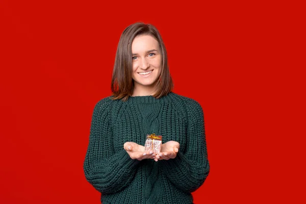Uśmiechnięta do kamery kobieta trzyma mały zapakowany prezent w dłoniach na czerwonym tle. — Zdjęcie stockowe