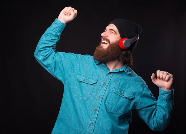 Feliz hombre barbudo sonriente escuchando música en auriculares inalámbricos y bailando sobre fondo oscuro — Foto de Stock