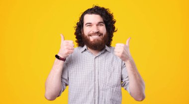 Uzun saçlı ve sakallı mutlu beyaz adam başparmağını kaldırıyor ve kameraya gülümsüyor.