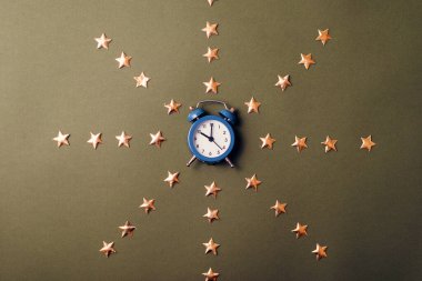 Çalar saat, altın yıldızların ortasında, karanlık masanın üzerinde duruyor.