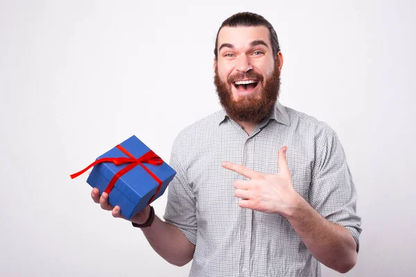 A very excited man is holding a gift pointing at it is looking at the camera