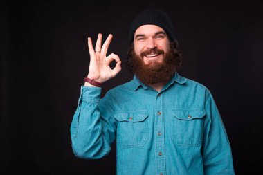 Genç, sakallı, mutlu bir adamın, kameraya gülümseyen ve karanlık bir duvarın yanındaki 