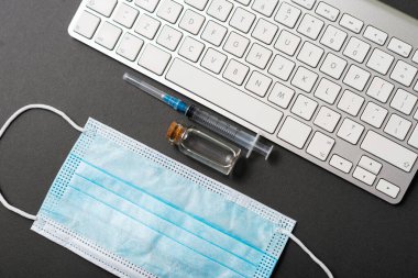Bir maske, aşı ve karanlık bir masanın üzerinde klavye fotoğrafı.