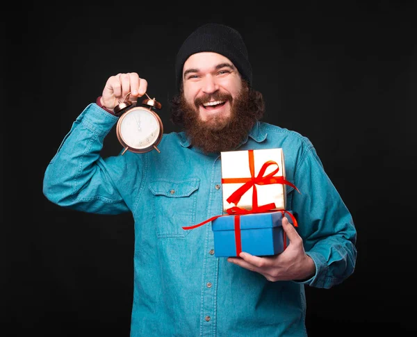 Ένας ενθουσιασμένος νεαρός γενειοφόρος κρατάει δώρα και ένα μικρό ρολόι που δείχνει ότι ο χρόνος τους τελειώνει. — Φωτογραφία Αρχείου