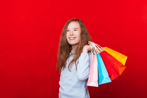 Веселый ребенок, девушка держит сумки для покупок и глядя в сторону на красный фон — стоковое фото
