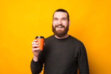 Neşeli, yakışıklı, sakallı bir adam bir fincan kahve içiyor sarı arka plandan alıp götürüyor.