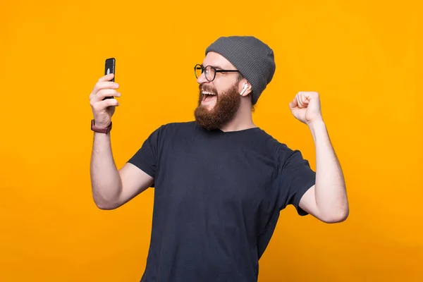 Foto de homem hipster barbudo espantado olhando para smartphone e celebrando — Fotografia de Stock