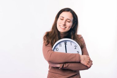 Genç, gülümseyen bir kadın duvar beyaz saatini kucaklıyor..